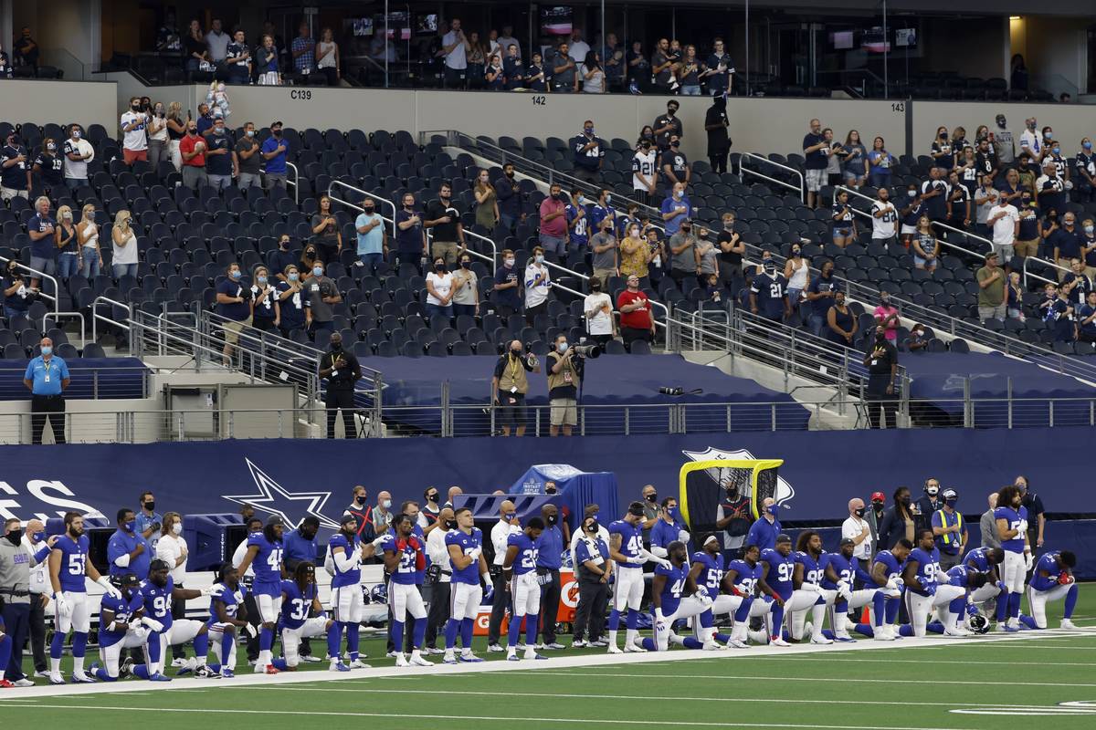 Players and staff of the New York Giants stand and kneel as they and fans in attendance listen ...