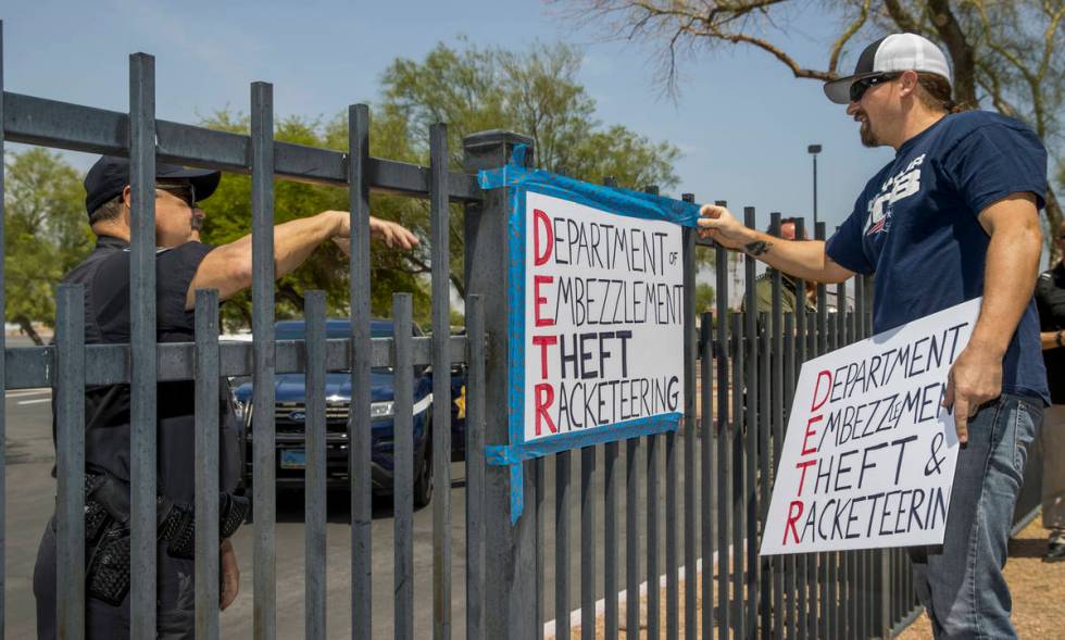 A security guard instructs Jon Berry, right, to take down a sign he attached to a fence in fron ...