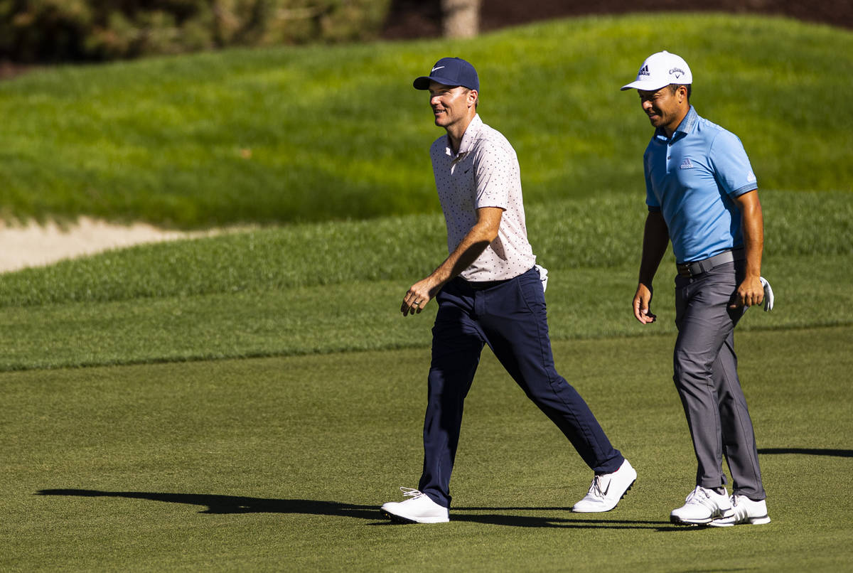 Russell Henley, left, talks with Xander Schauffele as they walk on the fairway at the 12th hole ...