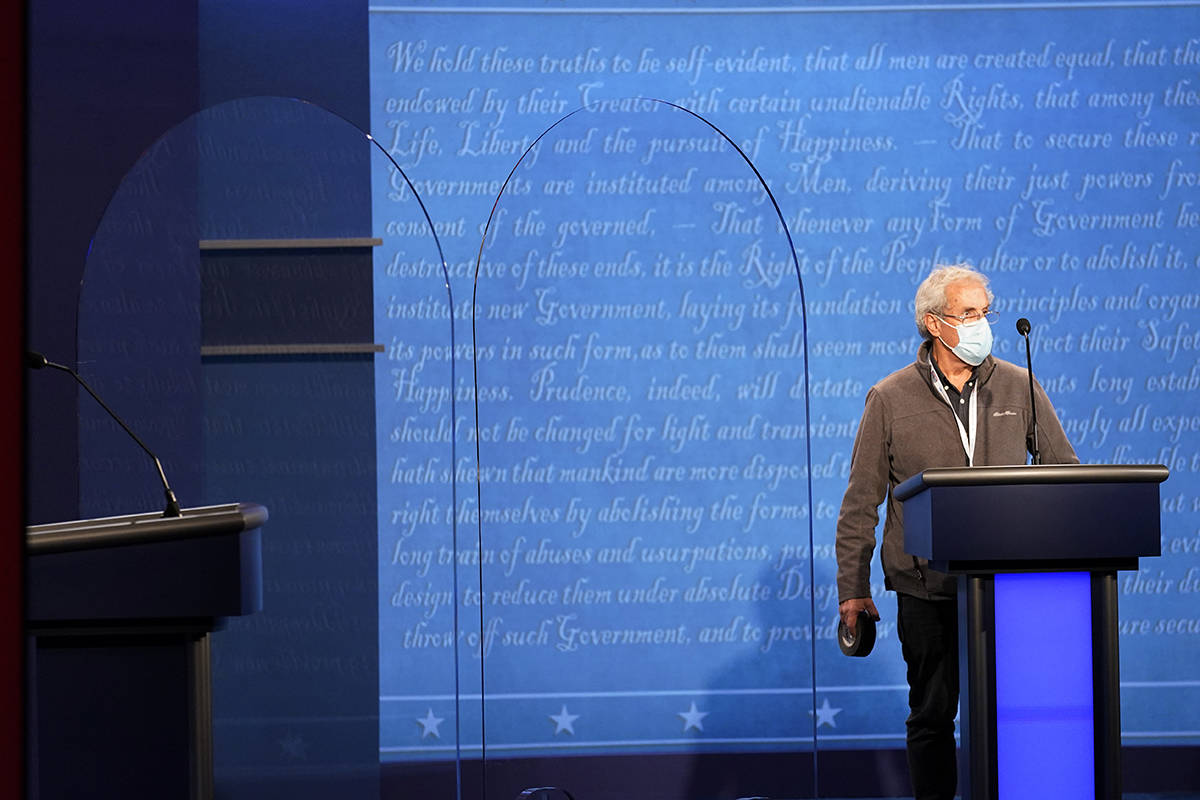 A member of the production crew stands at a podium near glass barriers to prevent the spread of ...