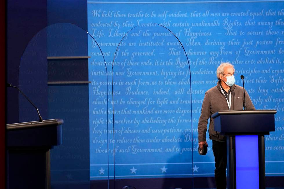 A member of the production crew stands at a podium near glass barriers to prevent the spread of ...