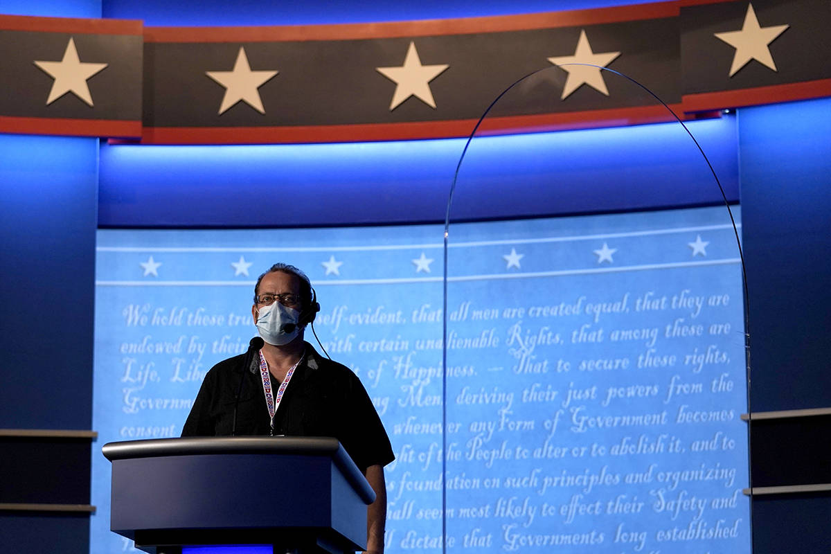 A member of the production crew stands at a podium near a glass barrier to prevent the spread o ...