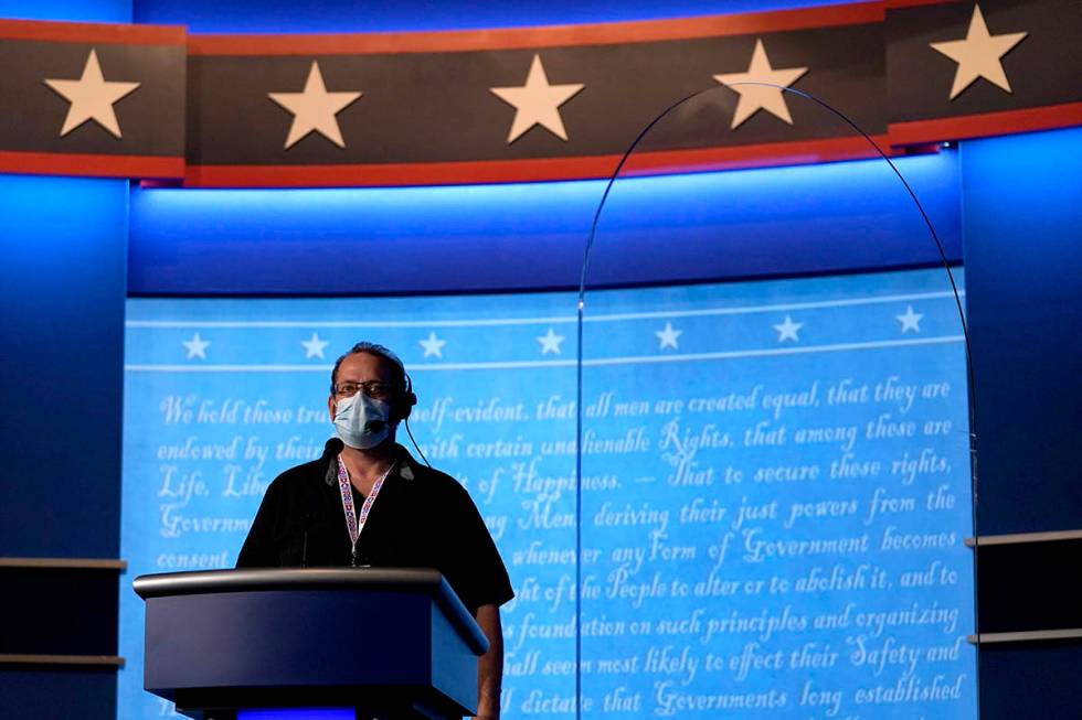 A member of the production crew stands at a podium near a glass barrier to prevent the spread o ...