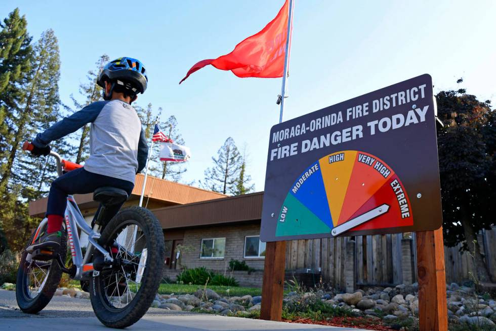 A boy rides his bike past the fire danger meter showing extreme fire danger in front of the Mor ...