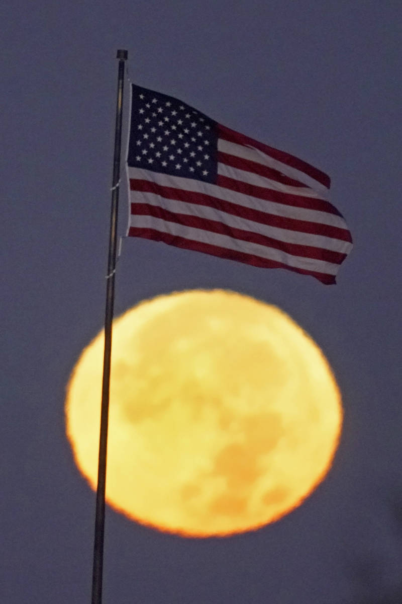 The full blue moon sets beyond an American flag Saturday, Oct. 31, 2020, in Kansas City, Mo. (A ...