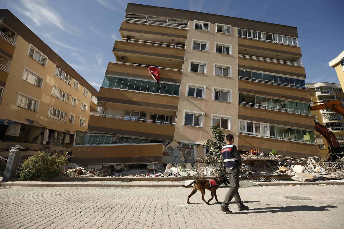 A member of rescue services with a dog, walks past a destroyed building in Izmir, Turkey, Sunda ...