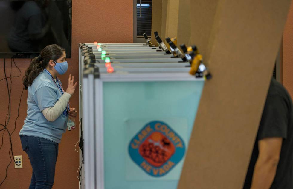 An elections worker gives instructions to a voter while in a booth with lights above showing th ...