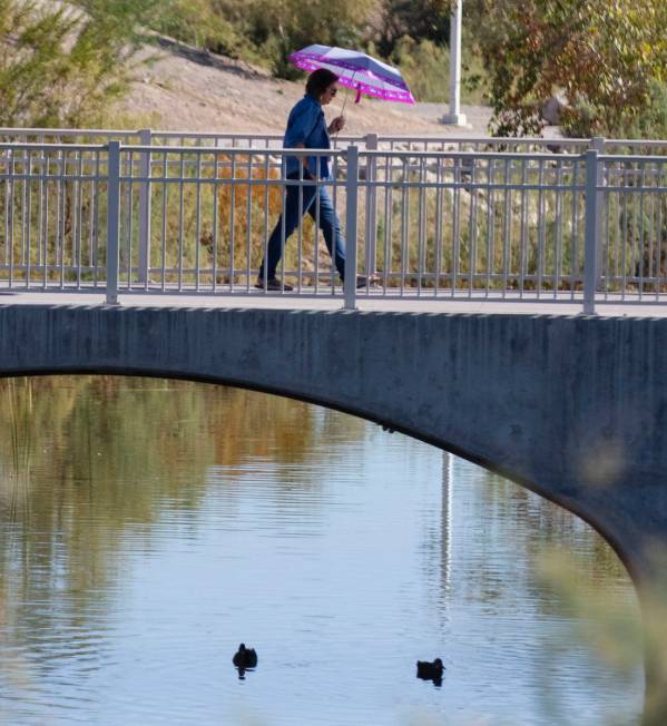 A woman holds an umbrella to protect herself from sun as she walks on pedestrian bridge at Corn ...