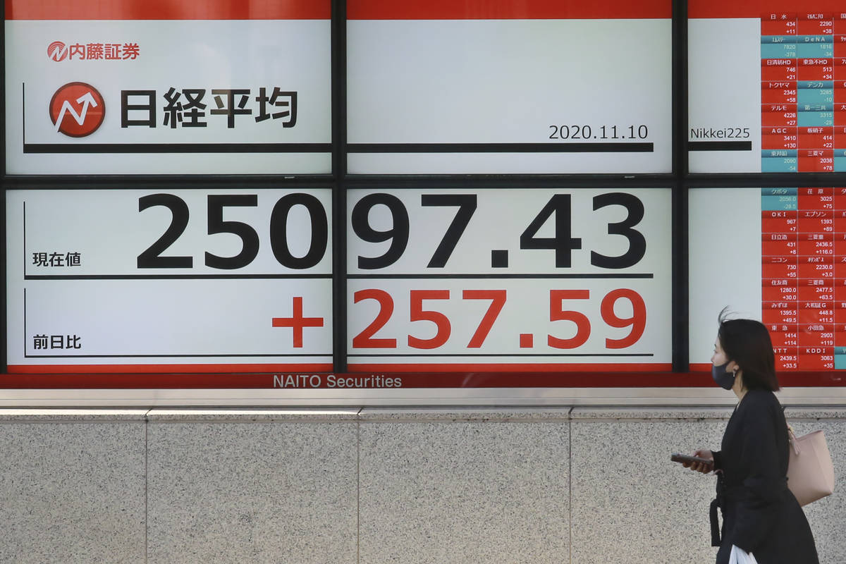 A woman walks by an electronic stock board of a securities firm in Tokyo, Tuesday, Nov. 10, 202 ...