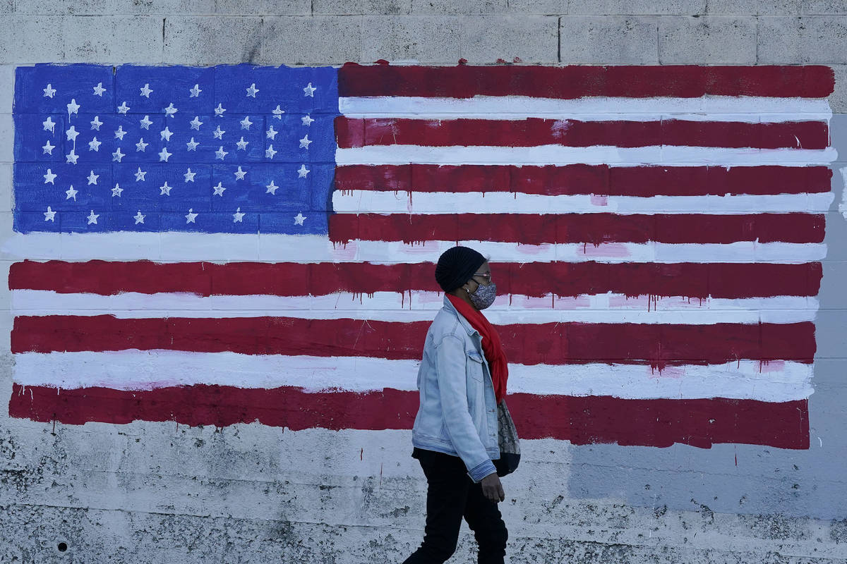 In this Nov. 16, 2020, file photo, a woman wears a mask while walking past an American flag pai ...