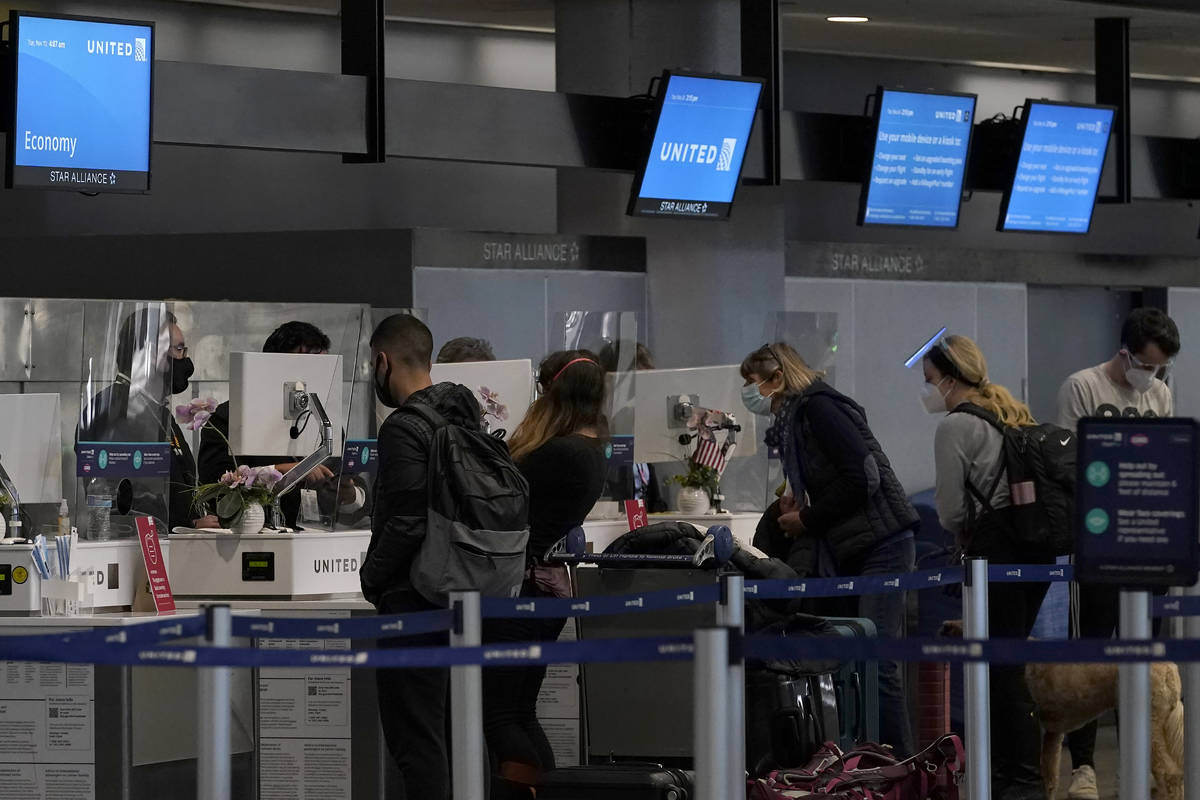 Travelers wearing masks check in at United desks at San Francisco International Airport during ...