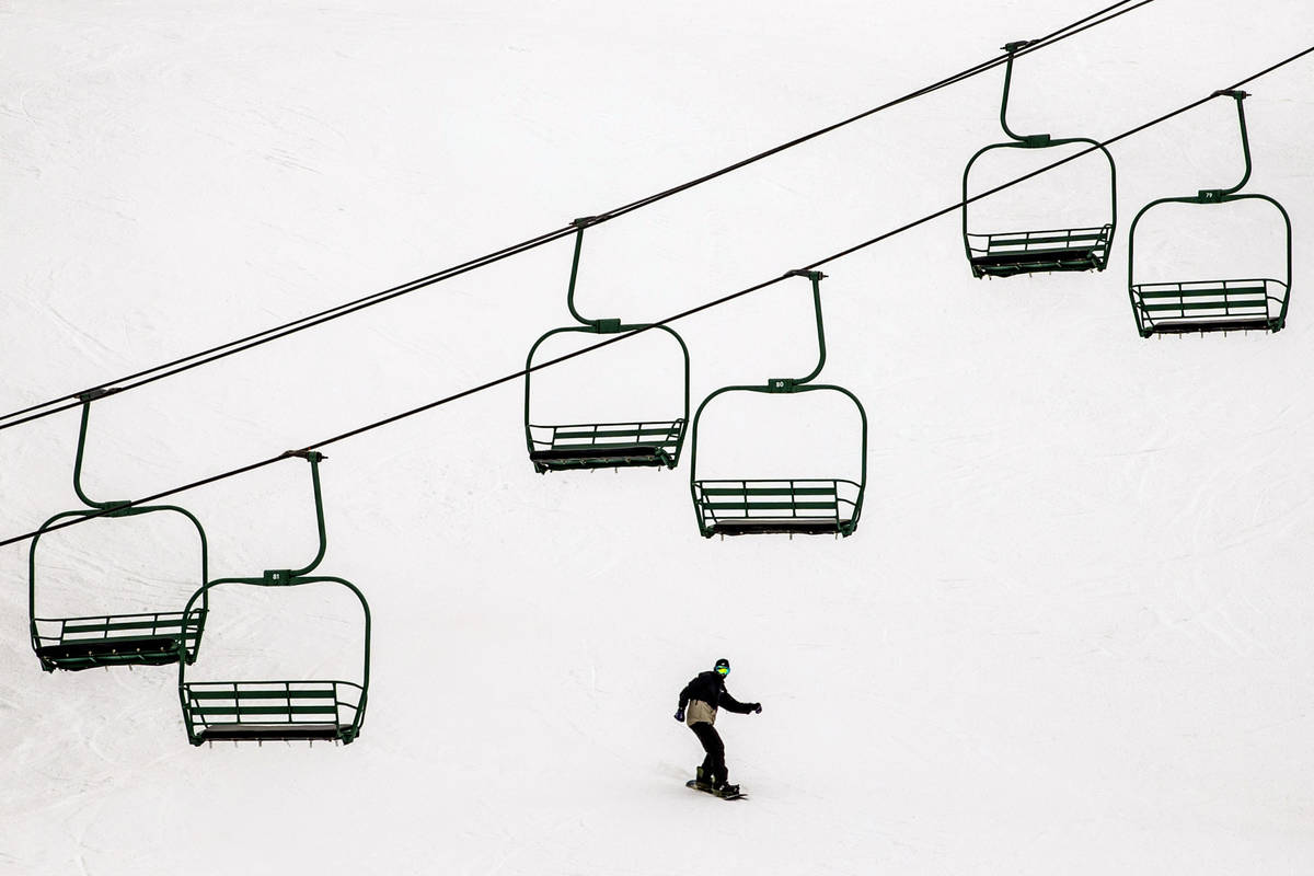 A snowboarder glides below empty chairs on a lift during opening day of skiing and snowboarding ...