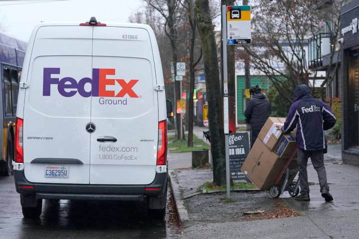 A driver with FedEx carries a package away from a van, Tuesday, Dec. 8, 2020, in Seattle. Store ...
