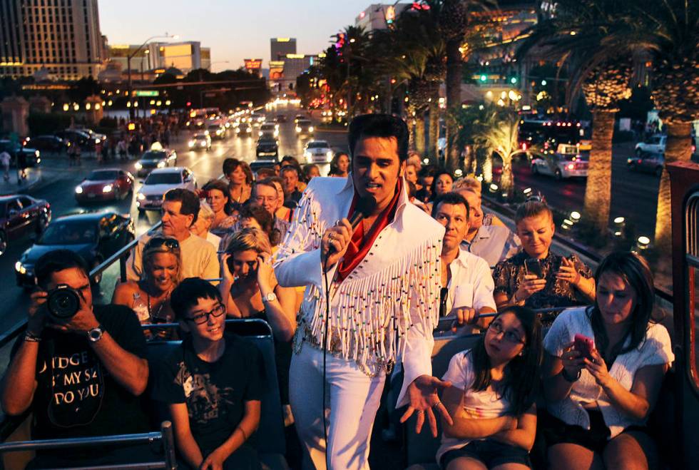 Elvis impersonator Steve Connolly performs on top of an open air double decker bus while travel ...