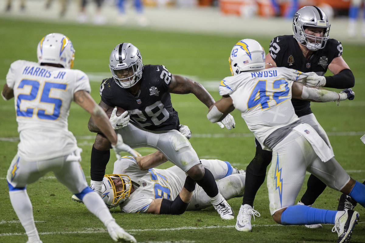 Raiders running back Josh Jacobs (28) tries to break free from Los Angeles Chargers cornerback ...