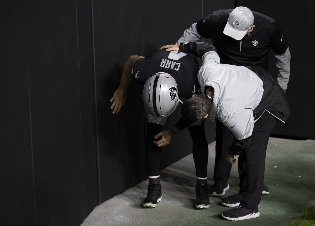 Raiders quarterback Derek Carr (4) hunches over while talking to training staff after getting h ...