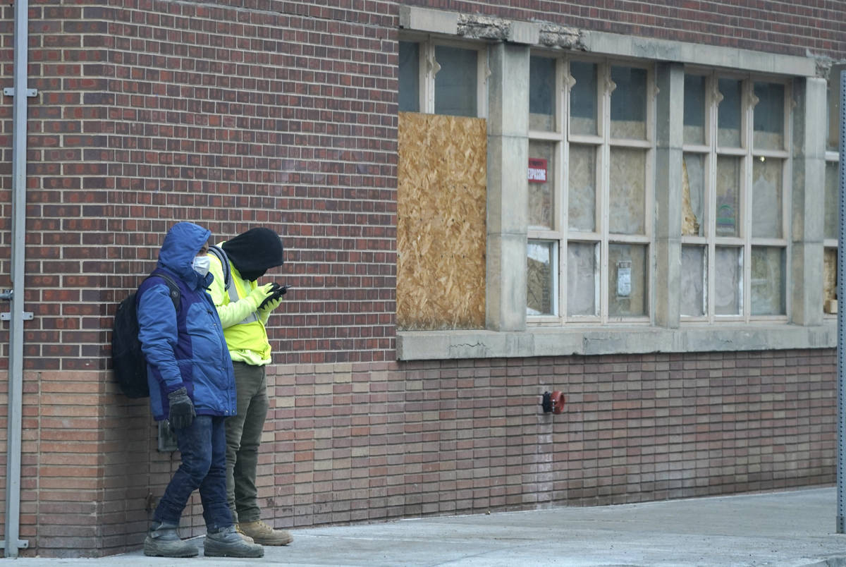 A pair of workers wear masks while waiting for a ride outside a construction site late Monday, ...