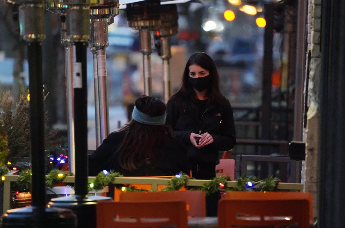 A waitperson wears a face mask while tending to a patron sitting in the outdoor patio of a sush ...