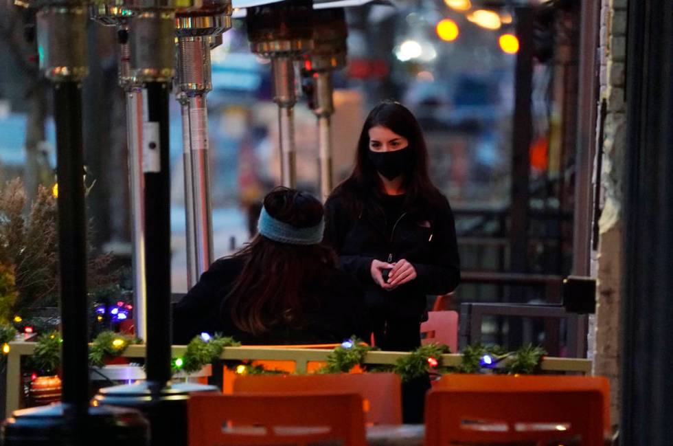 A waitperson wears a face mask while tending to a patron sitting in the outdoor patio of a sush ...