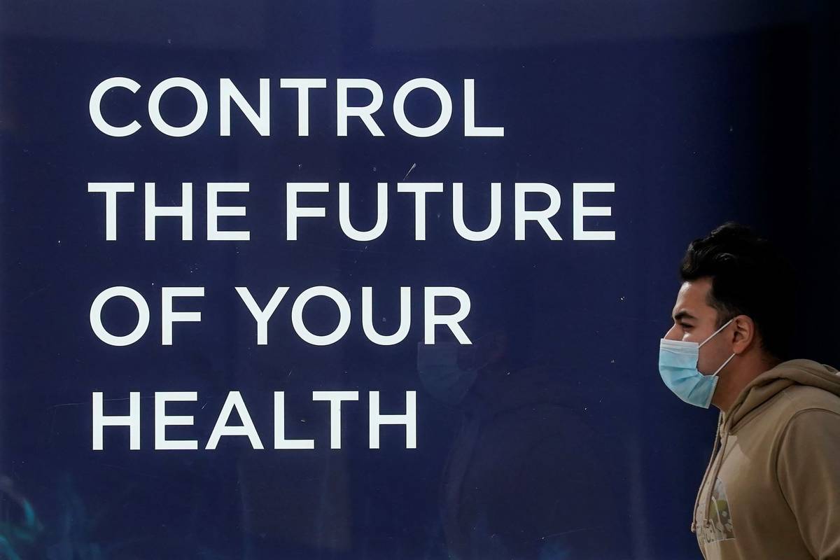 A pedestrian wears a face mask while walking past a sign at a Forward healthcare location durin ...