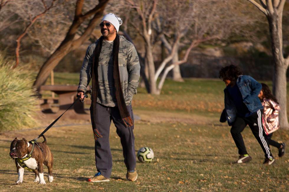 Orlando Farias walks his dog, Freddie, while his children play soccer in the background at Expl ...
