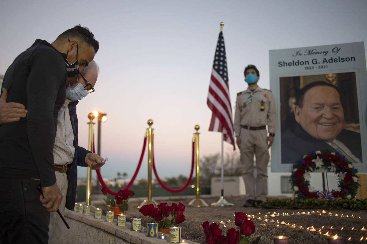 Lior Gal, left, embraces Neville Pokroy as they pay their respects to Sheldon Adelson by lighti ...