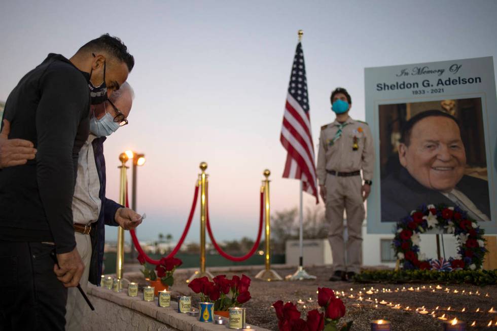 Lior Gal, left, embraces Neville Pokroy as they pay their respects to Sheldon Adelson by lighti ...