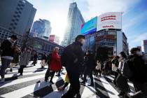 People wearing protective masks to help curb the spread of the coronavirus walk along pedestria ...