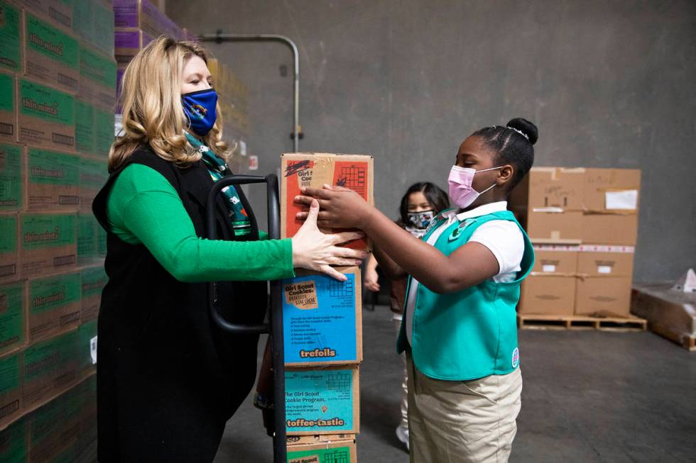 Girl Scout Aliyah H., 9, moves a box of Girl Scout Cookies onto a dolly held by Kimberly Trueba ...