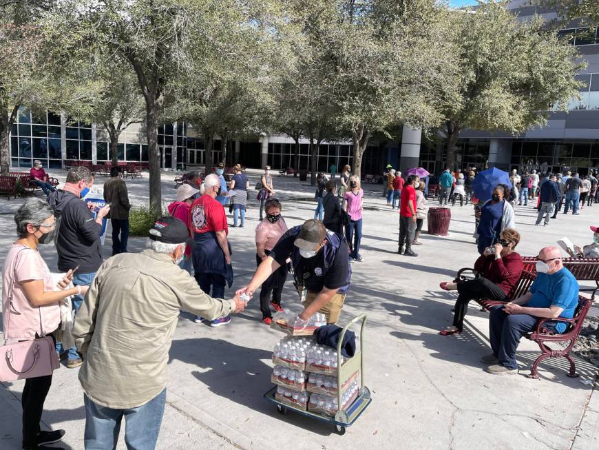 A worker hands out water to people in line for the second dose of the COVID-19 vaccine outside ...