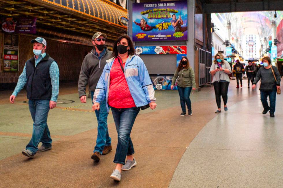 People wearing face masks, including two worn improperly below the nose, are seen walking along ...