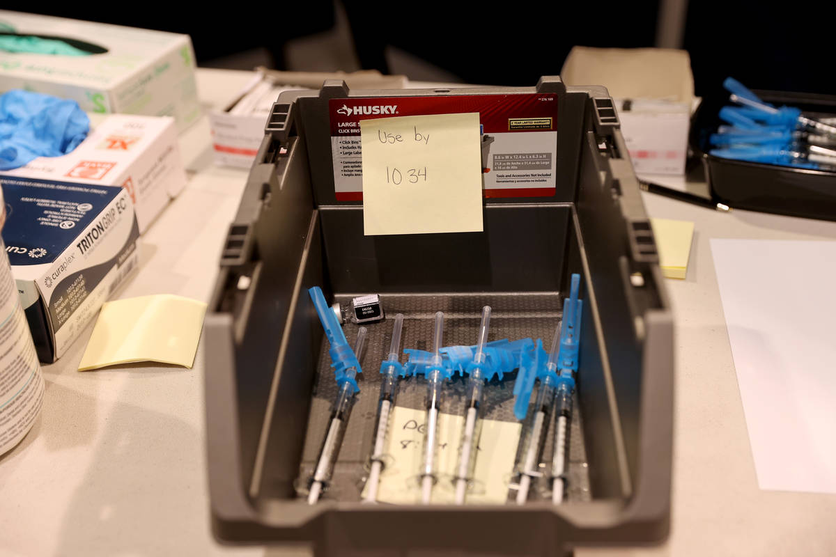 Syringes with Pfizer vaccines in a bin with a "use by" label at the Cashman Center COVID-19 vac ...