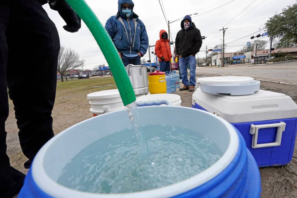 A water bucket is filled as others wait in near freezing temperatures to use a hose from public ...