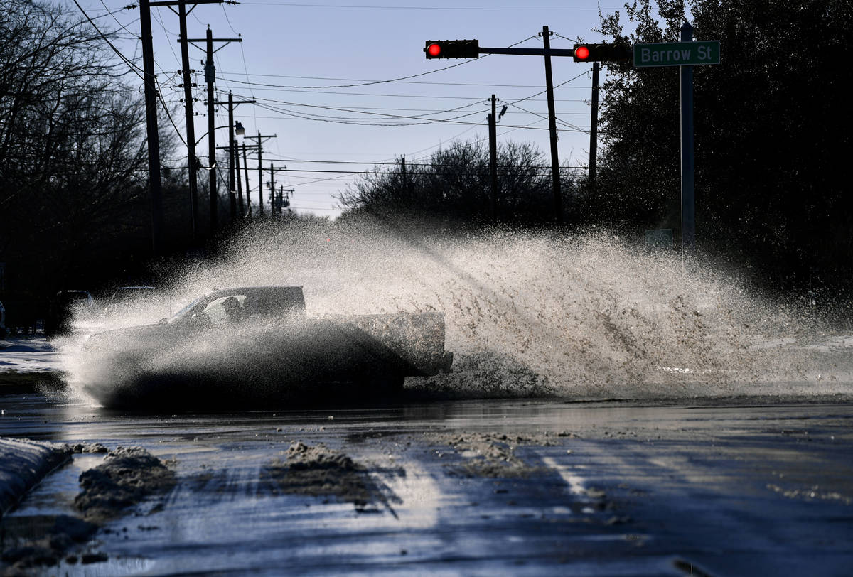 A pickup sends a wake of snow melt high into the air as the driver plows through a large puddle ...