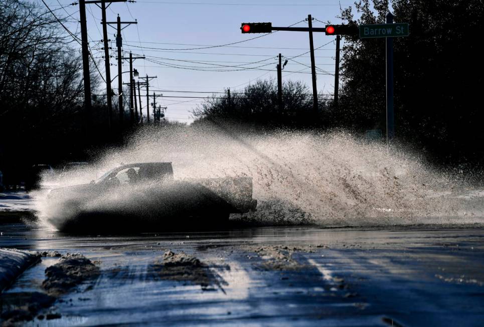 A pickup sends a wake of snow melt high into the air as the driver plows through a large puddle ...