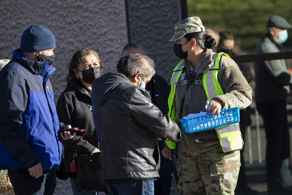 A member of the national guard passes out wristbands to people waiting in line for their COVID- ...