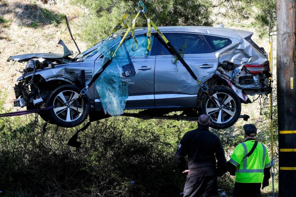 Workers watch as a crane is used to lift a vehicle following a rollover accident involving golf ...