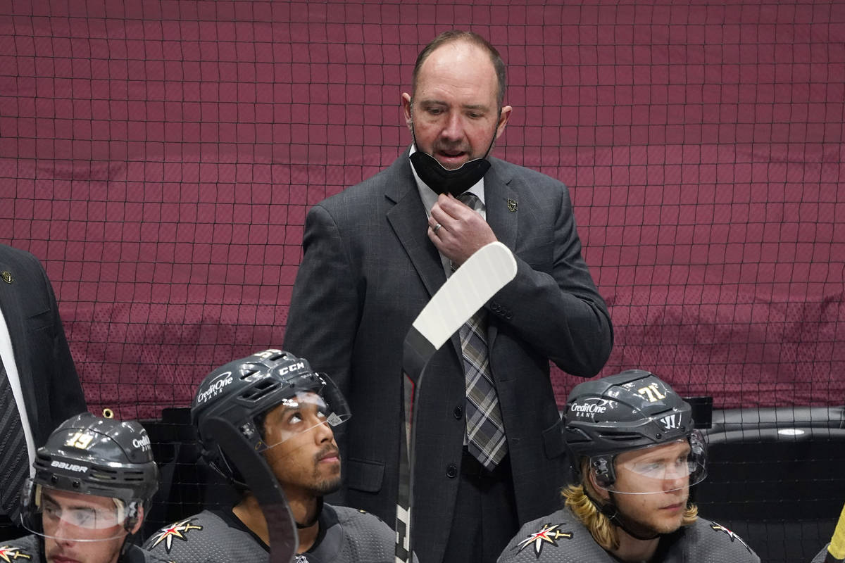 Vegas Golden Knights head coach Peter DeBoer, back, pulls down his mask to talk to his players ...