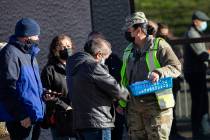 A National Guard member passes out wristbands to people waiting in line for their COVID-19 vacc ...