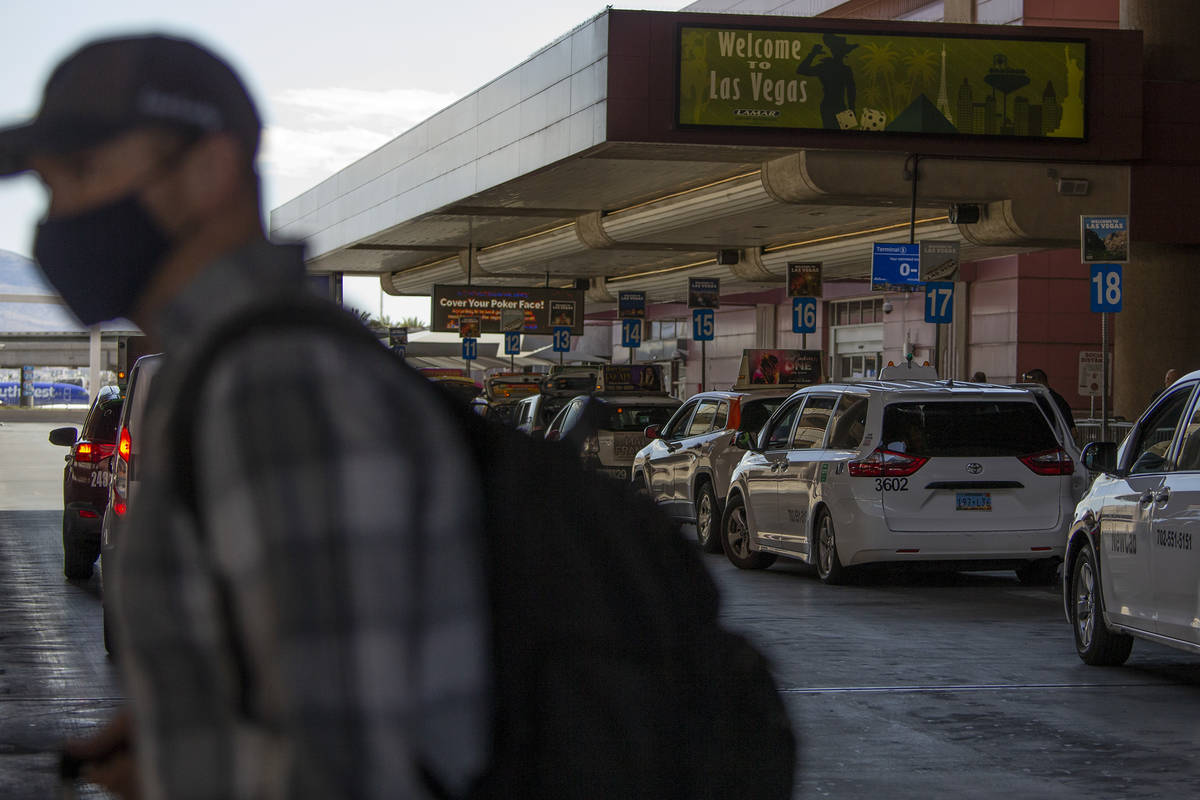 A masked person exits McCarran International Airport as taxis line up to take visitors to their ...