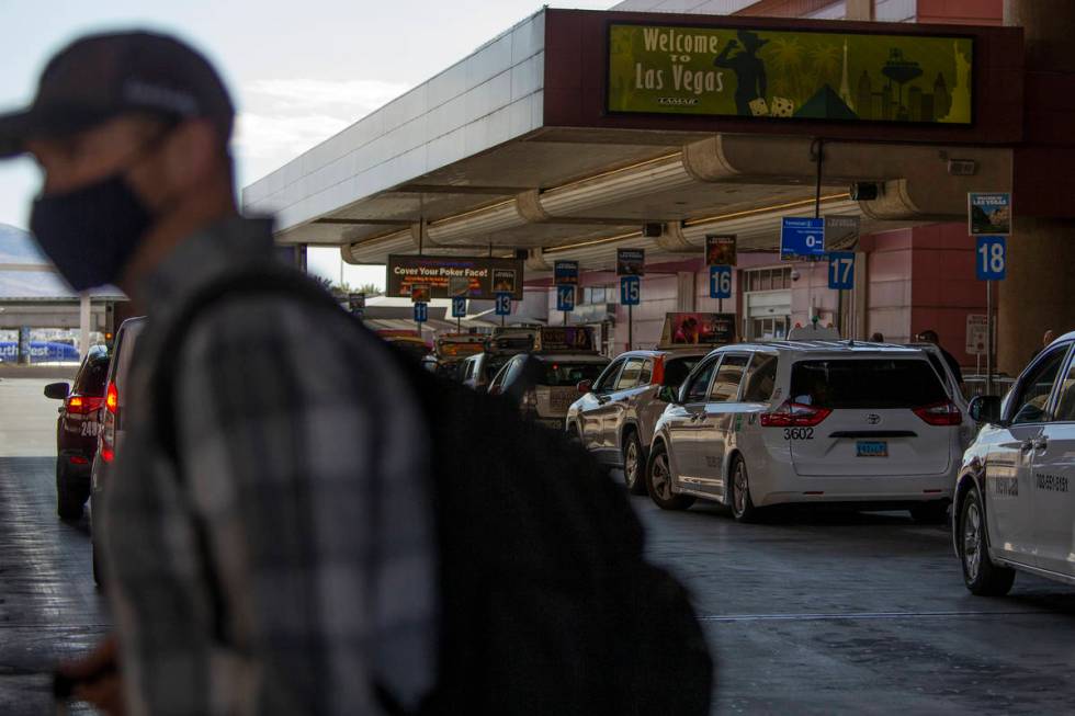 A masked person exits McCarran International Airport as taxis line up to take visitors to their ...