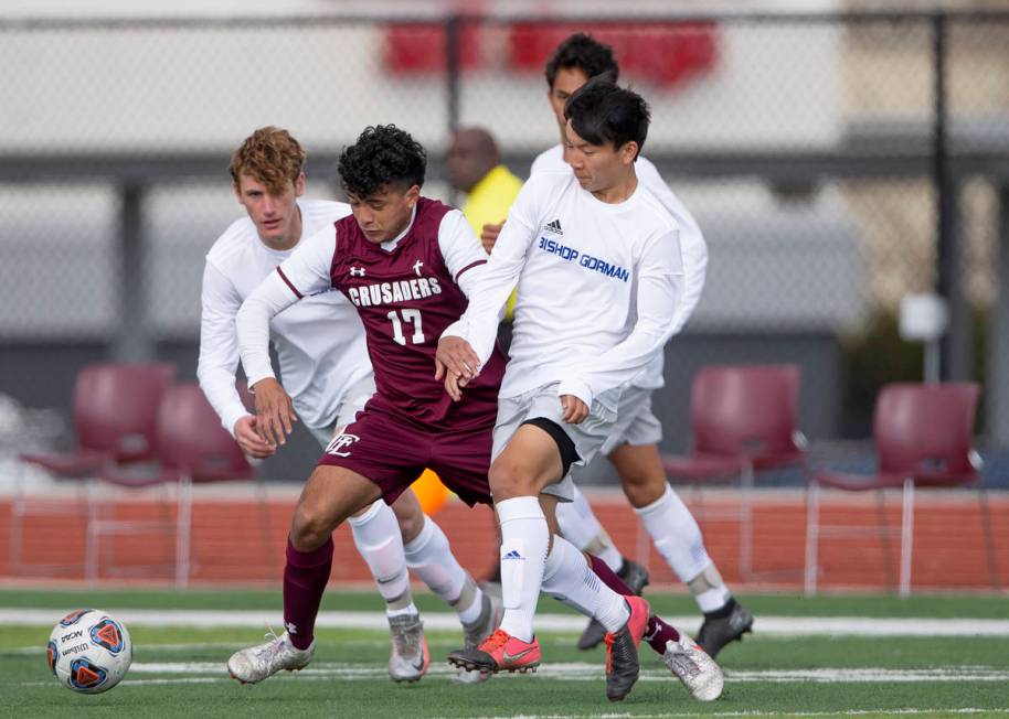 Faith Lutheran midfielder Preston Rincon (17) runs for the ball flanked by Bishop Gorman Nathan ...