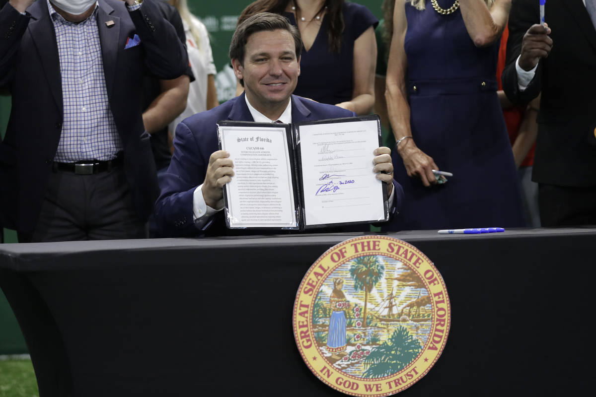 Florida Gov. Ron DeSantis holds up a signed bill which would allow college athletes in the stat ...