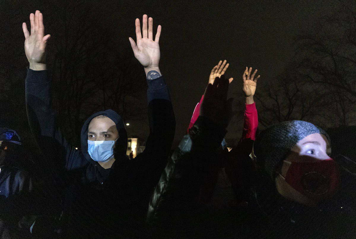 People hold up their hands as a crowd gathers at the Brooklyn Center Police Department, late Su ...