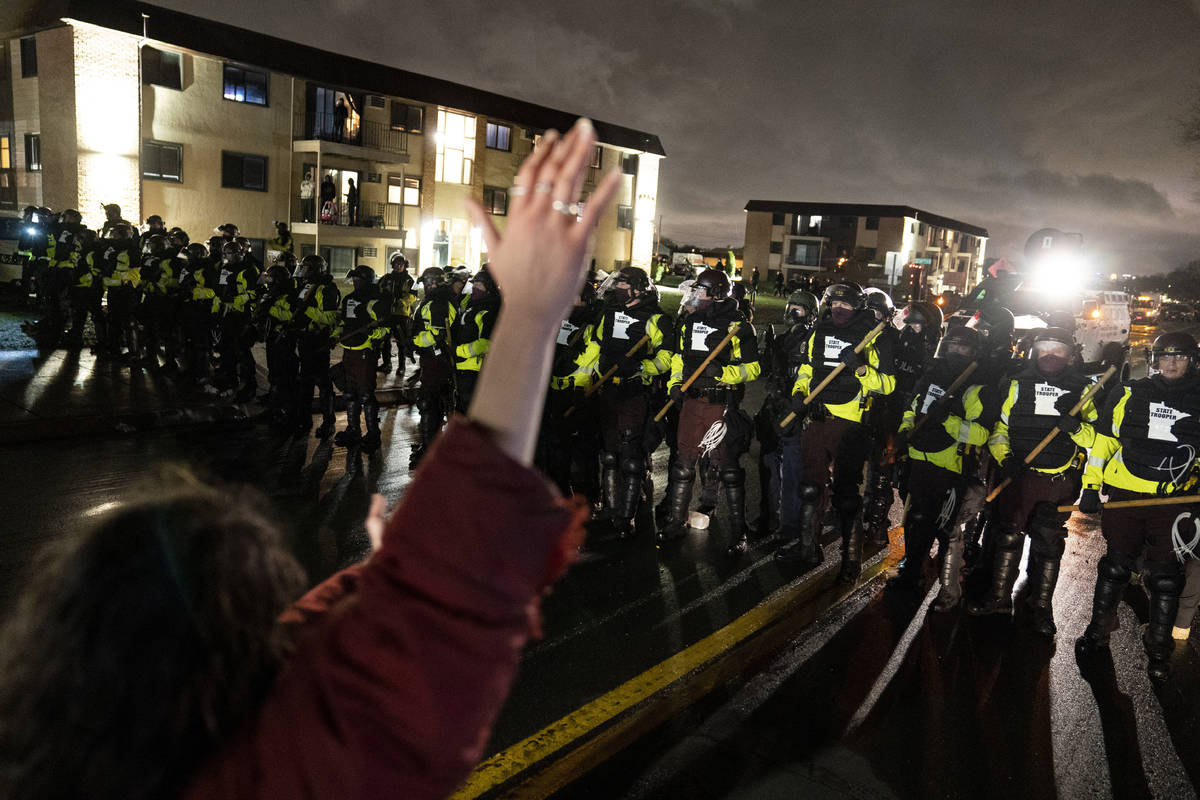 A demonstrator raises their hand while facing off against a perimeter of police as they defy an ...