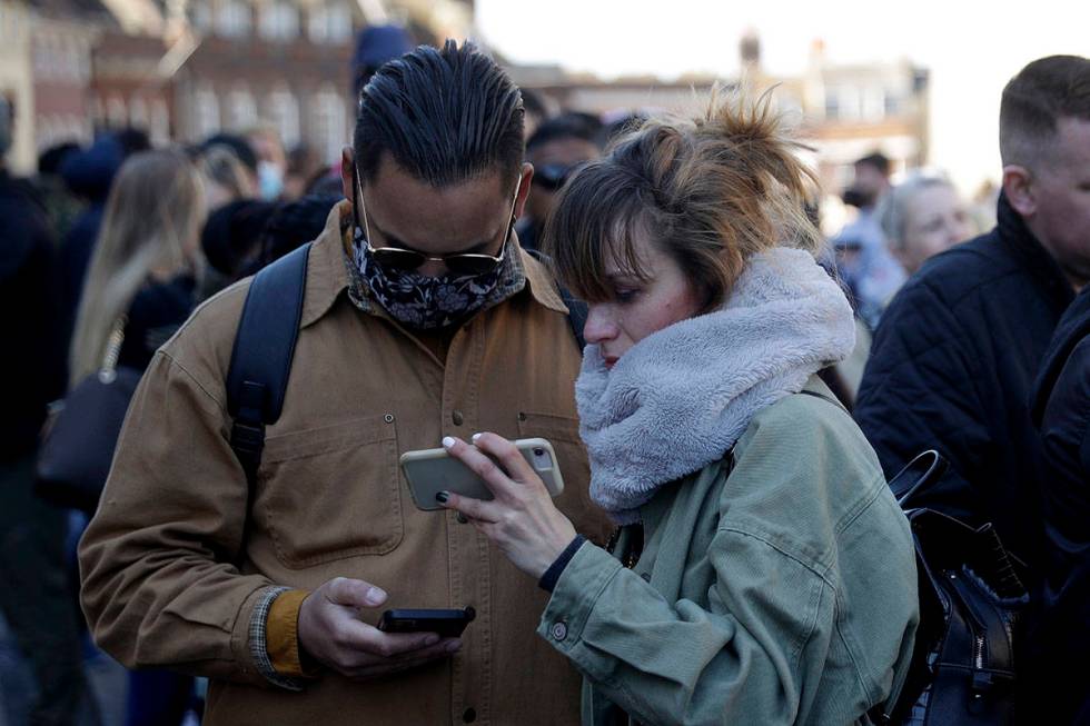 People watch live coverage on a phone outside Windsor Castle during the funeral of Britain's Pr ...