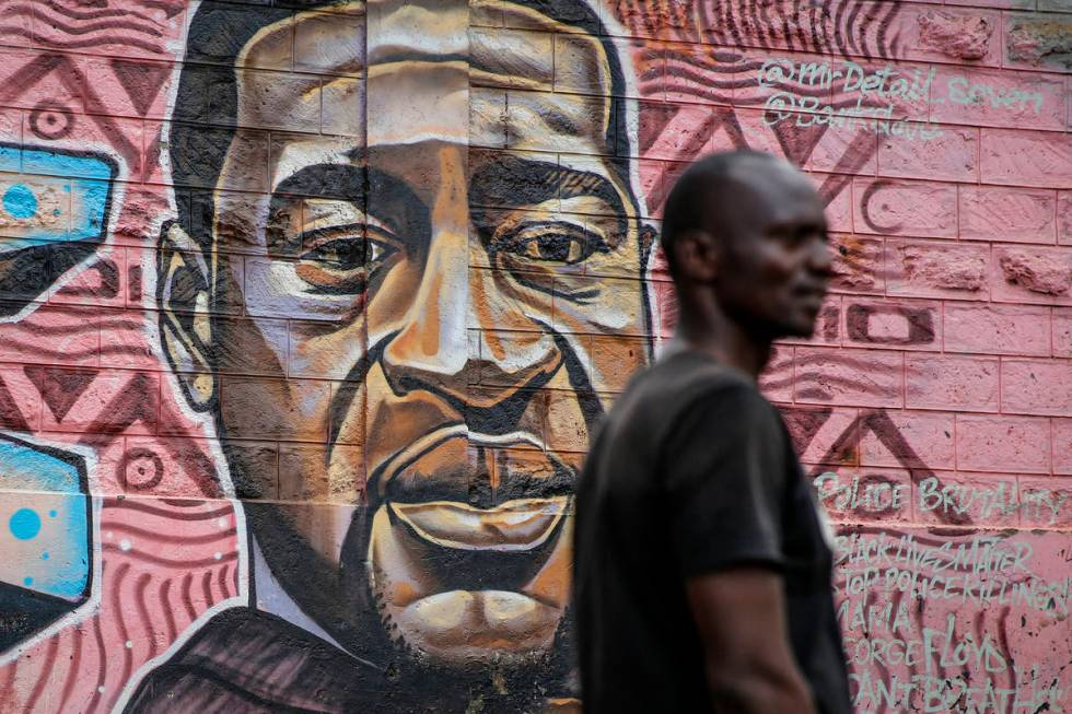 A local resident stands next to a mural painted in June 2020 showing George Floyd with the Swah ...