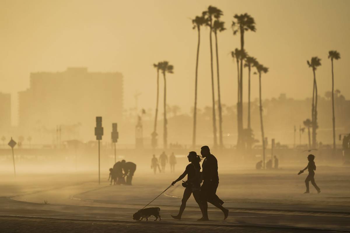 People walk on a beach path as evening winds kick up sand in Long Beach, Calif., in April 2021. ...