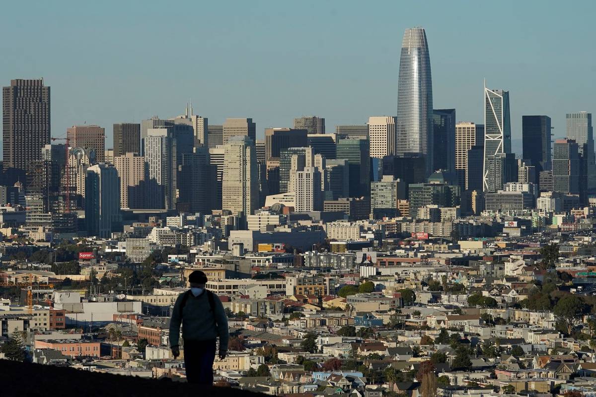 A person wearing a protective mask walks in front of the skyline on Bernal Heights Hill during ...