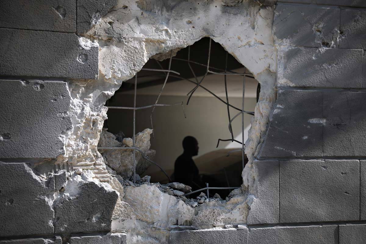 A man is seen trough a hole in a wall of a residential building after it was struck by a rocket ...